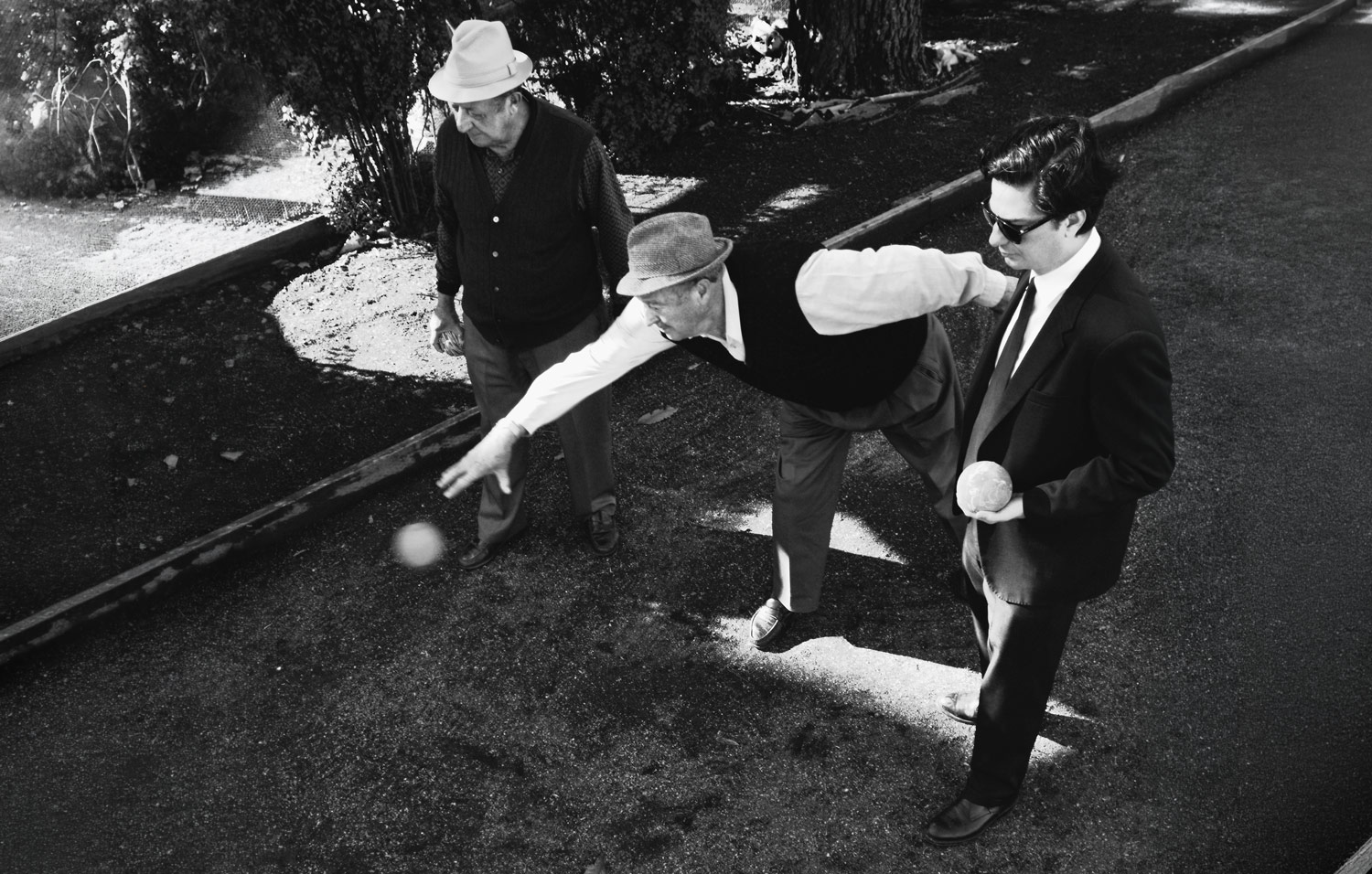 Black-and-white photograph of three men playing bocce