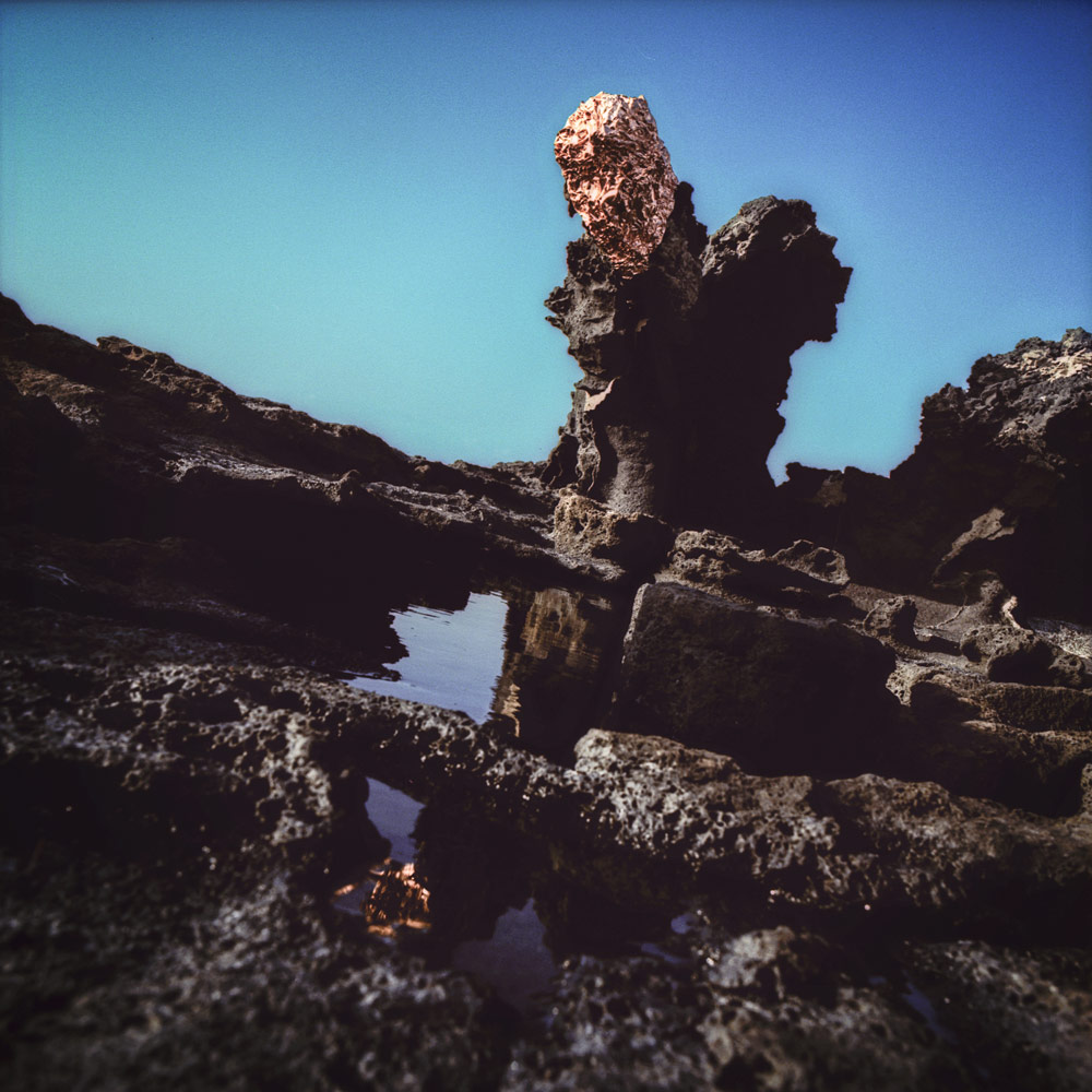 Copper atop a volcanic rock formation reflected in a tidal pool