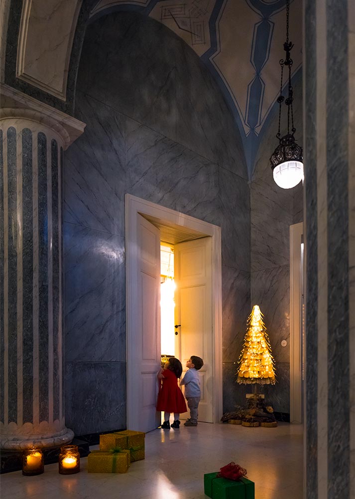 Two children beside a glowing doorway and a Christmas tree at Palazzo Margherita